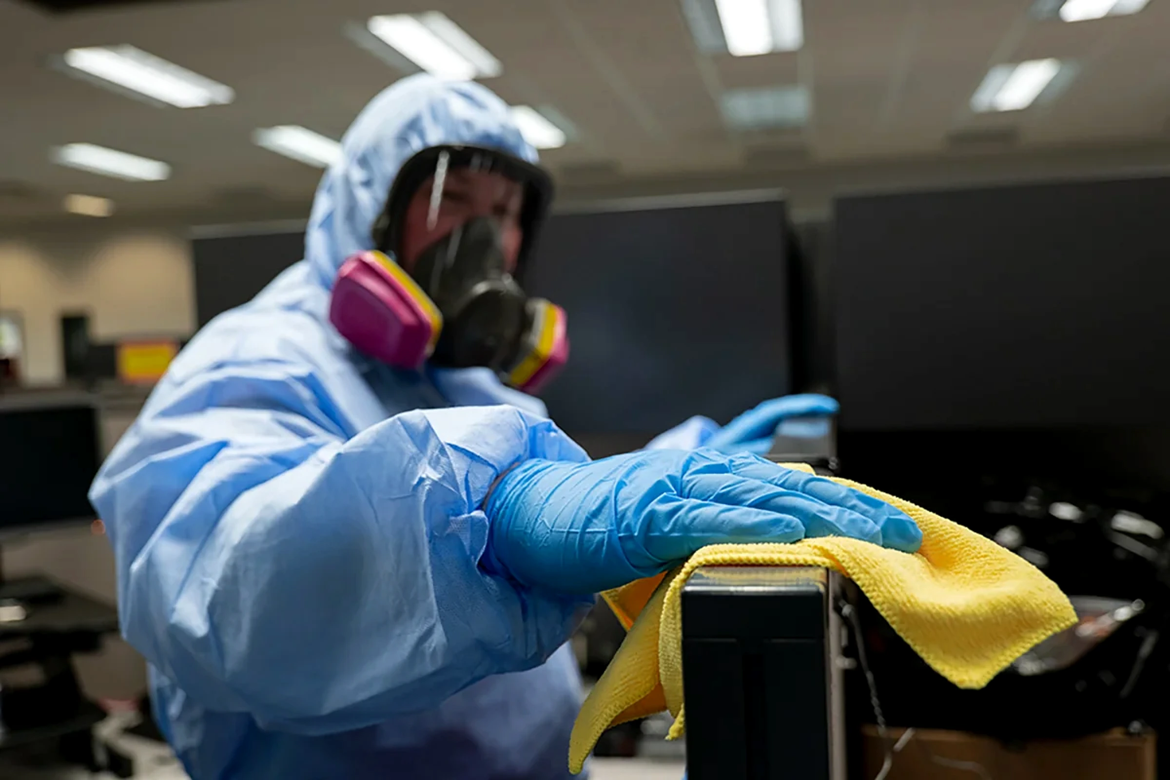 Worker in protective clothing wiping office equipment with a yellow cloth